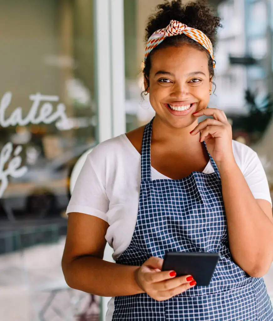Happy entrepreneur standing in her café, smiling and using a tablet pc for the day to day management of her coffee shop . Business woman embracing technology in her small business.