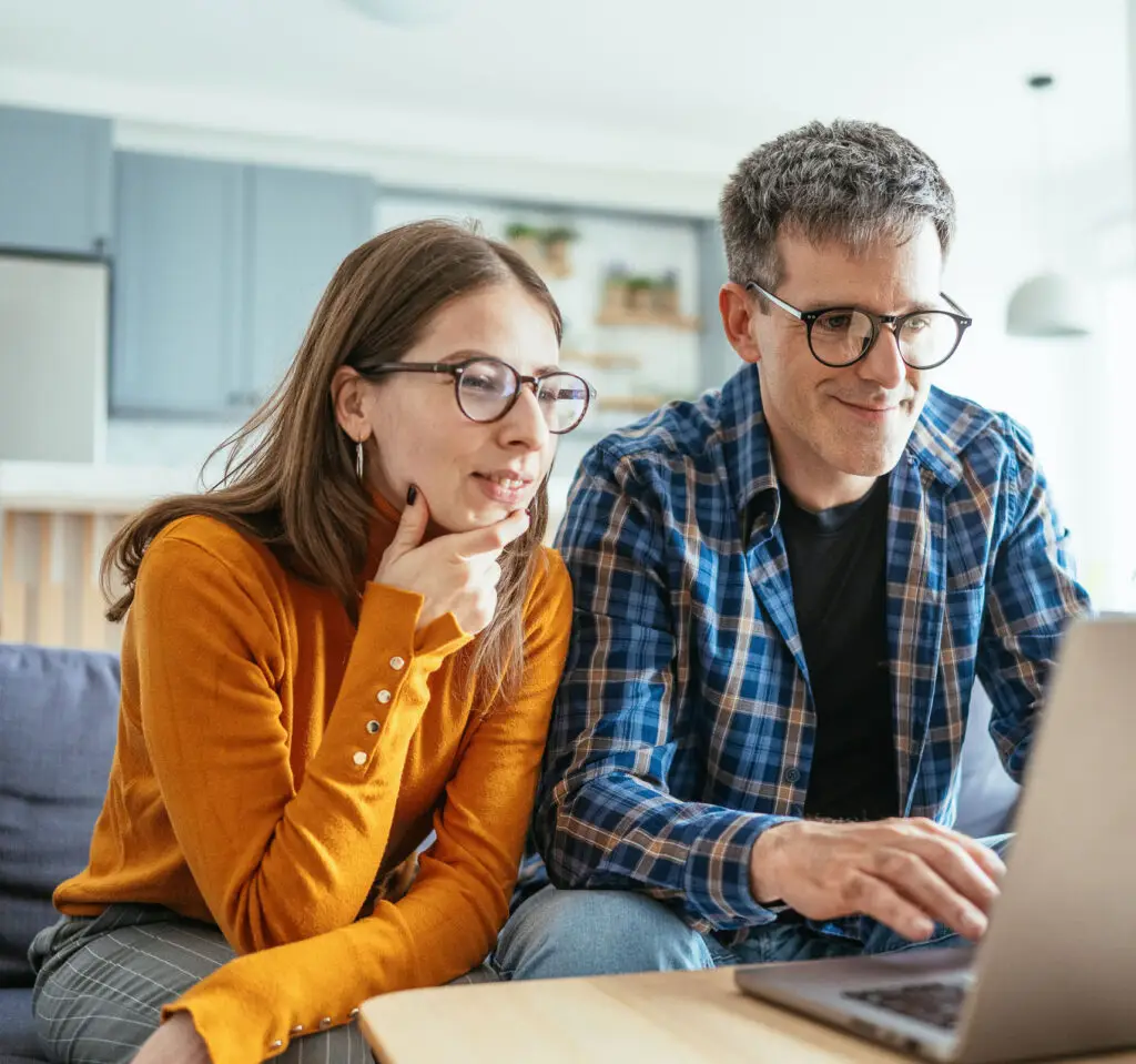 A couple sits comfortably on a couch with a laptop, enjoying quality time together in a modern, cozy living room setting